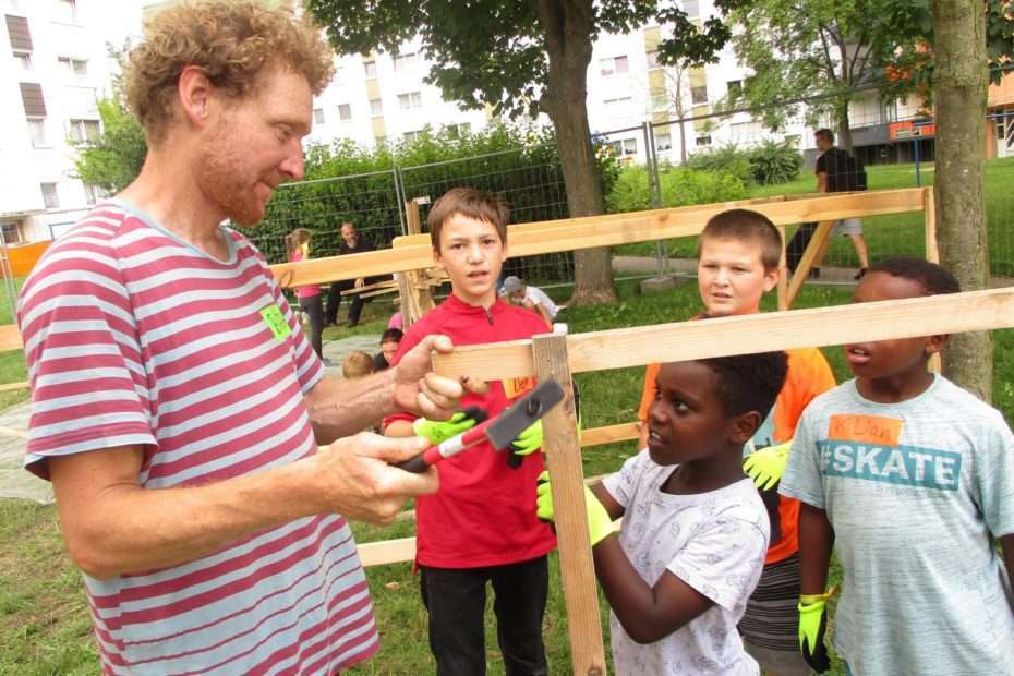 Kinder und ein Erwachsener mit Holz und Werkzeugen auf der Kidnerbaustelle in Prenzlau